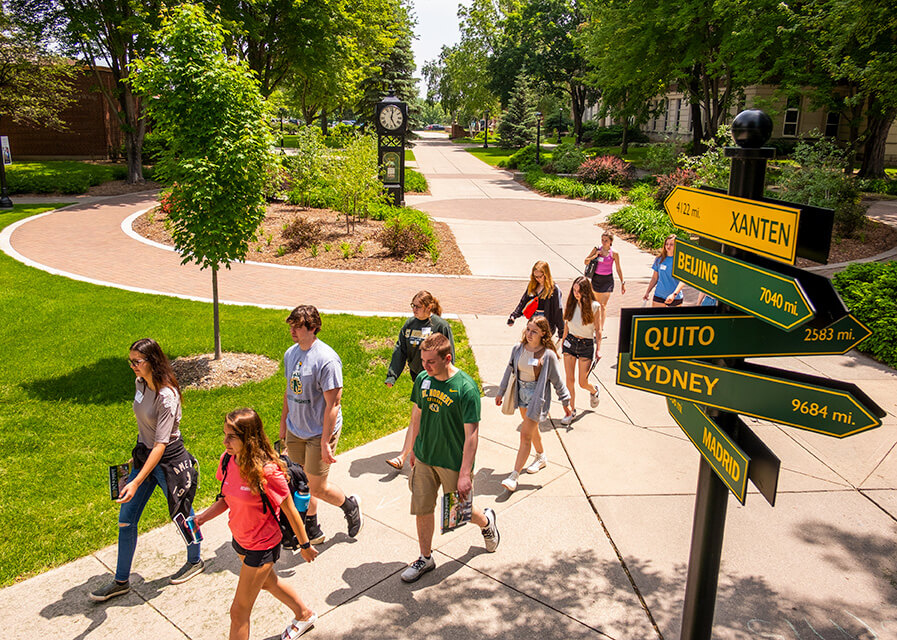 Students walk past directional signs pointing to Beijing, Quito, Sydney and Xanten. 