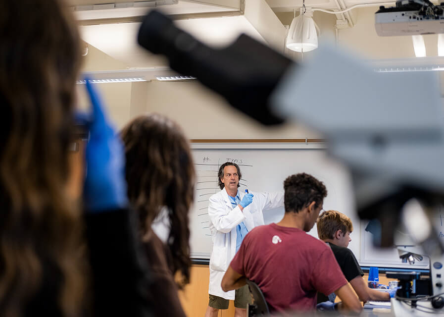 Professor wearing lab coat speaking in front of science lab